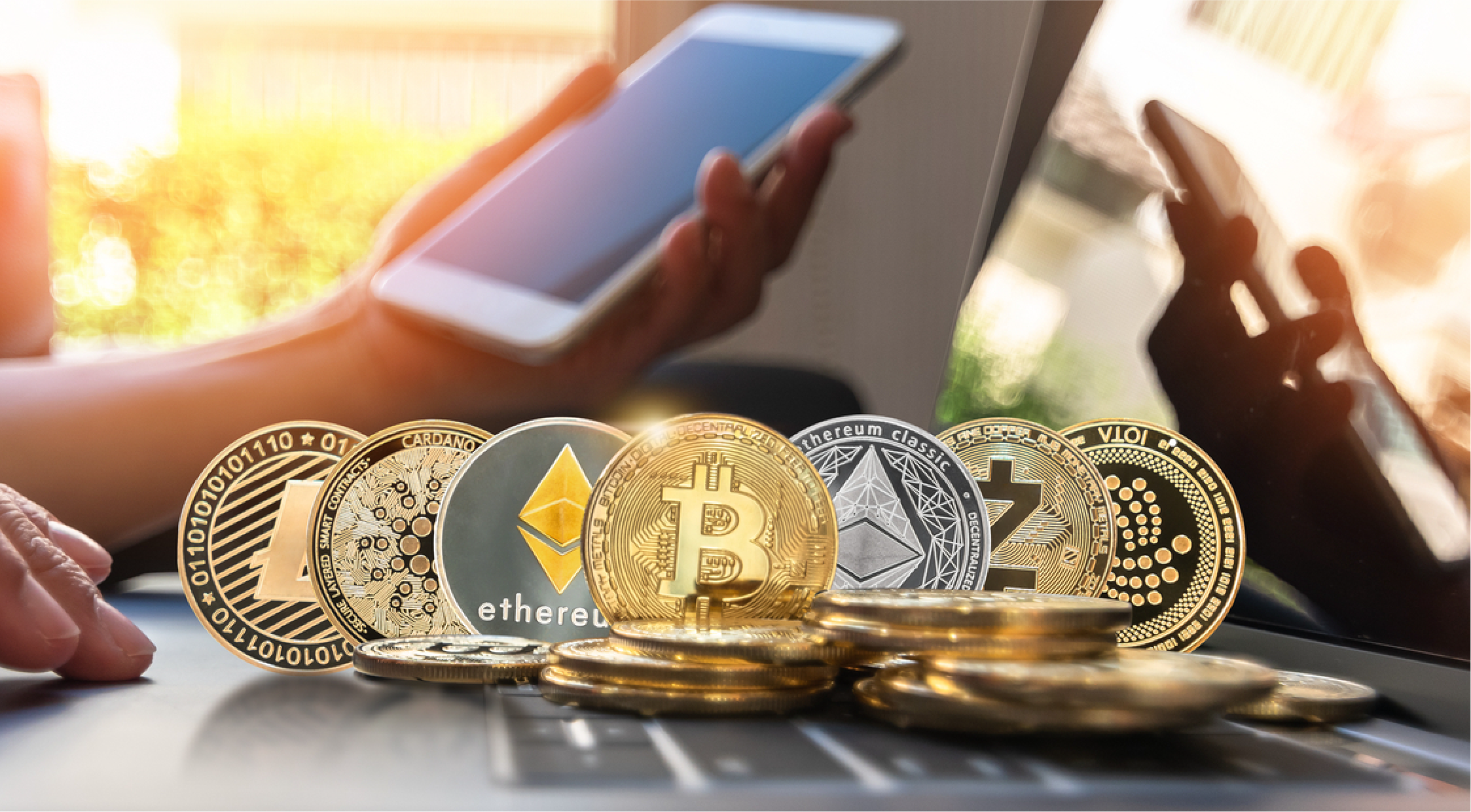 A row of cryptocurrency coins in front of a phone and laptop